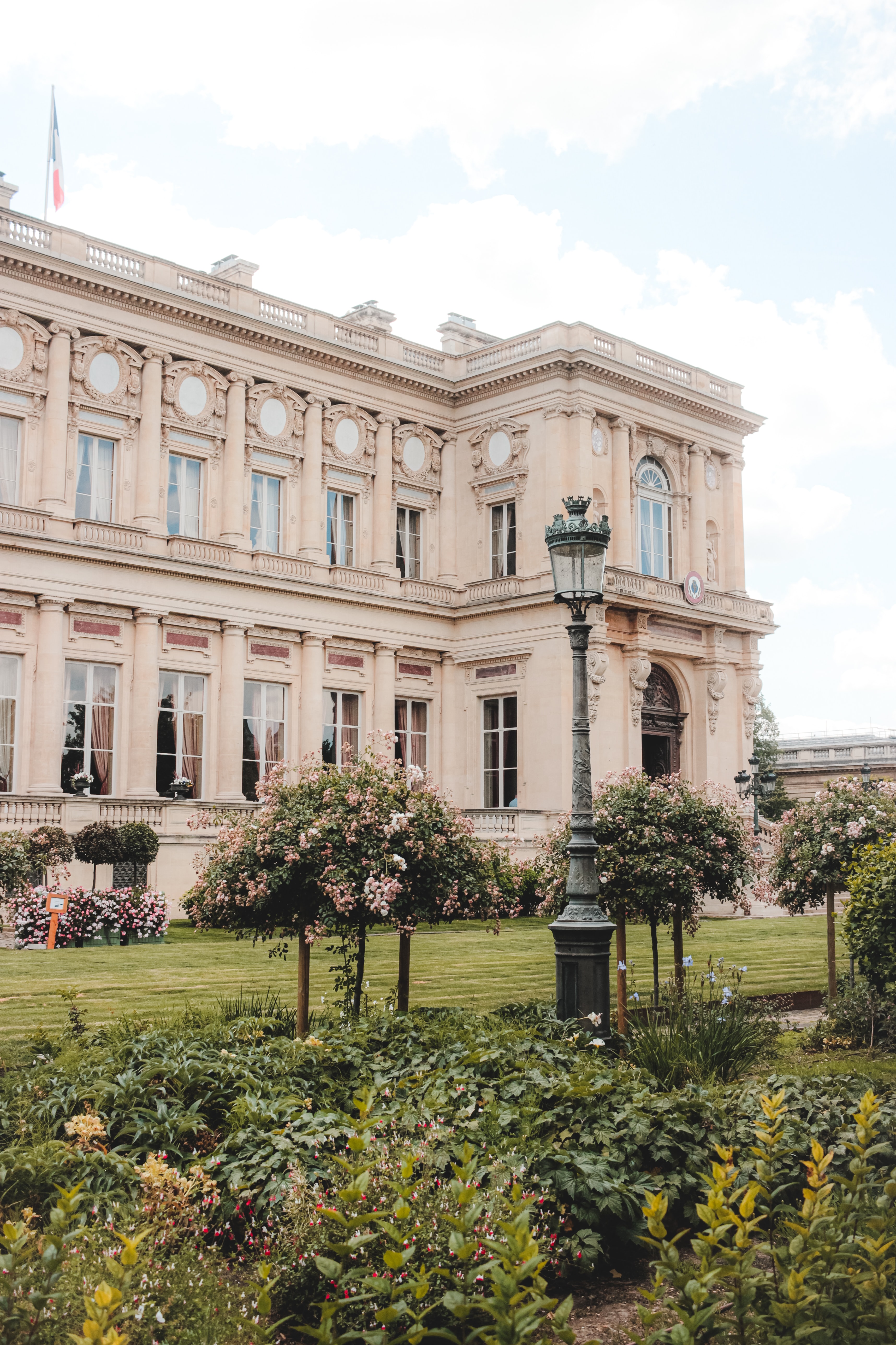 A white collegiate building with a green lampost and surrounded by beautiful gardens.